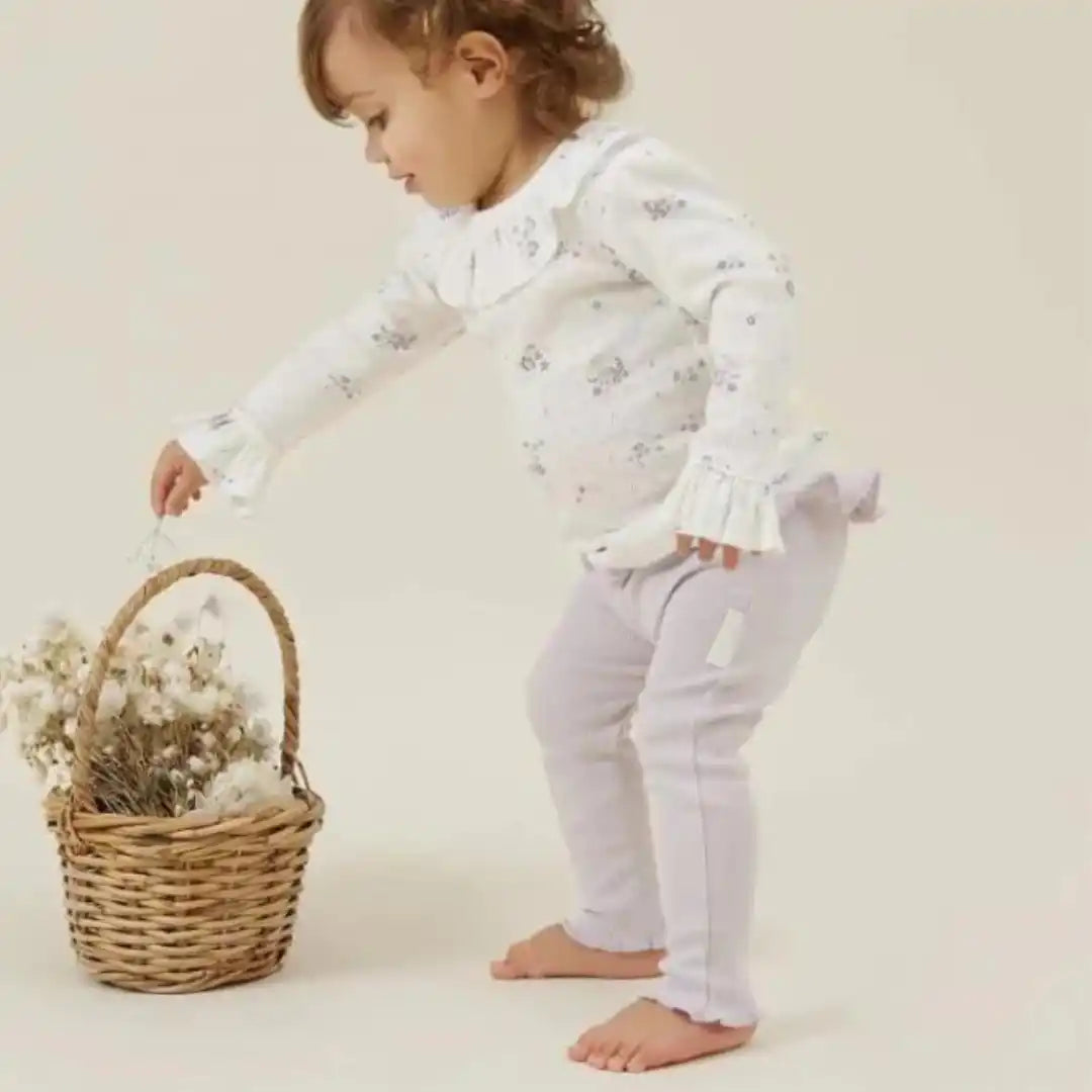 Toddler girl’s floral-patterned ruffled blouse and lavender leggings.